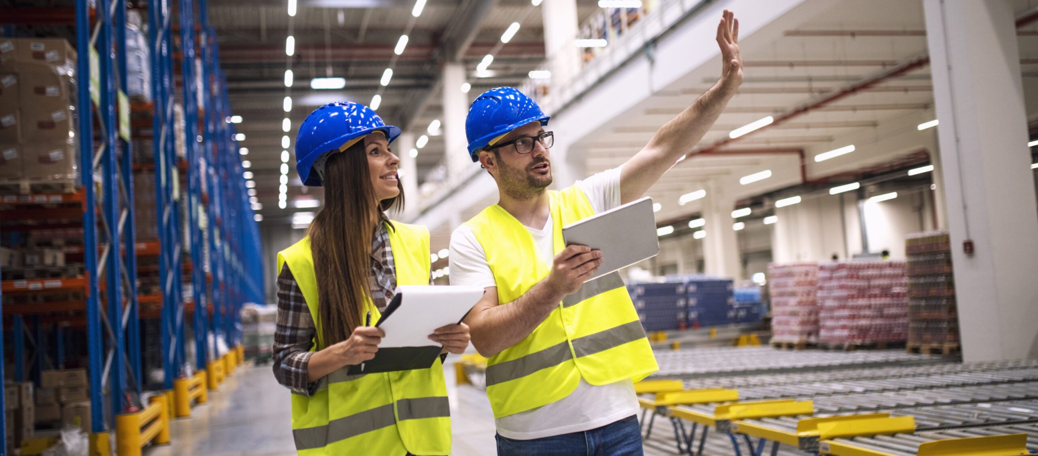 Warehouse workers consulting each other in large factory storage area.